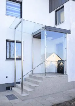 Individuell gefertigtes Glasvordach mit Seitenteil aus Sicherheitsglas und Edelstahlkonstruktion über modernem Hauseingang.